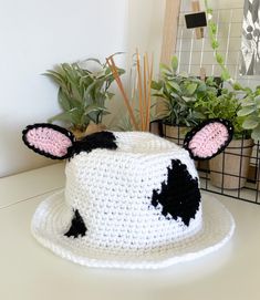 a crocheted cow hat sitting on top of a table next to potted plants