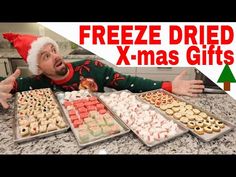 a man wearing a santa hat sitting at a table filled with trays of cookies