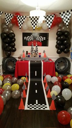 a birthday party with balloons and race car decorations on the wall, along with black and white checkered tablecloths