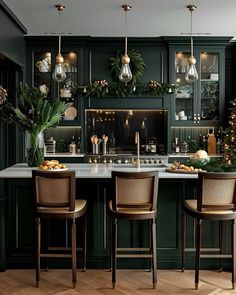 the kitchen is decorated for christmas with greenery and hanging lights on the cabinets, along with two bar stools