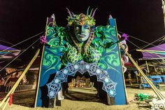 an elaborately painted sculpture on the beach at night time with people around it and umbrellas in the background