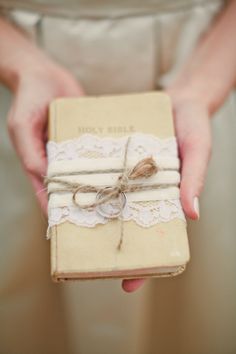 a person holding a small book wrapped in paper and twine with lace on it