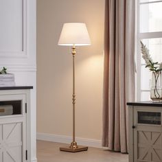 a floor lamp with a white shade on it in a room next to a window