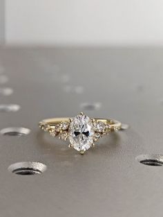 a close up of a ring on a surface with dots in the background and an oval shaped diamond surrounded by smaller round diamonds