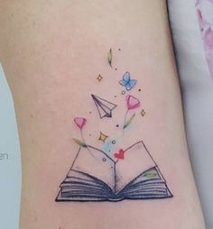 an open book with paper airplanes flying out of it on the side of a woman's leg