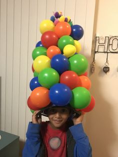 a young boy is wearing a bunch of balloons on his head