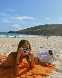 a woman laying on top of a beach holding a camera