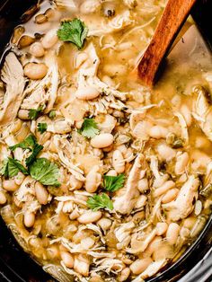 chicken and bean soup in a crock pot with a wooden spoon on the side