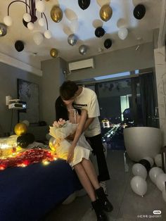 a man and woman kissing in front of a bed with balloons hanging from the ceiling