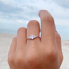 a woman's hand with a three stone ring on it, in front of the ocean