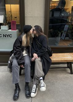 two women sitting on a bench in front of a nyc department store kissing each other