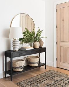 a black table with two baskets and a round mirror on top of it next to a rug