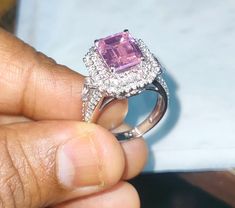 a person holding a ring with a pink stone in it's center and surrounded by white diamonds