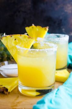 two glasses filled with pineapple margaritas on top of a wooden table