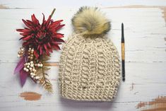 a crocheted hat with a pom - pom sits next to a flower