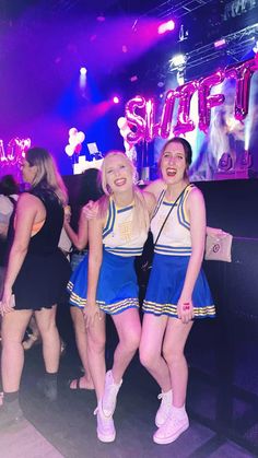 two young women in cheerleader outfits posing for the camera at a dance party with neon lights behind them