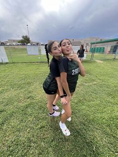 two girls in black shirts and shorts standing on grass with their arms around each other