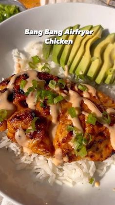 a white plate topped with chicken covered in gravy next to rice and avocado