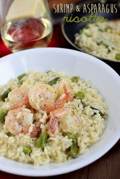 shrimp and asparagus risote in a white bowl next to a glass of wine