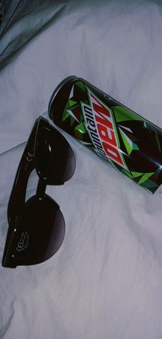 a can of soda and sunglasses on a bed