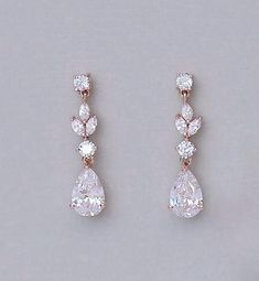 two pairs of diamond earrings on a gray surface with one earring in the shape of a tear