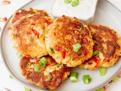 three crab cakes on a white plate with green onions and red peppers next to a bowl of ranch dressing