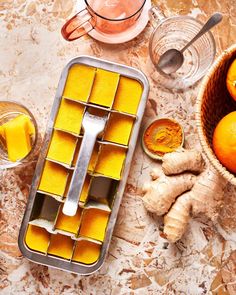 oranges and ginger ice cubes on a marble counter top with utensils