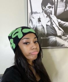 a woman with long hair wearing a green and black beanie next to a poster