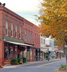 an old brick building on the corner of a street with autumn foliage in front of it