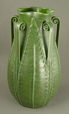 a large green vase with intricate designs on it's sides and bottom, sitting in front of a gray background