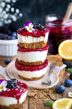 three layered cheesecakes with berries and blueberries on a plate next to lemon slices