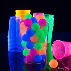 plastic cups with neon colored balls in them on a black background, one is empty