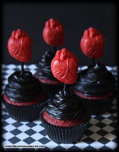 four cupcakes with chocolate frosting and red hearts on top are sitting on a checkered tablecloth