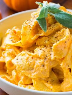 a white bowl filled with pasta next to an orange and green leafy garnish