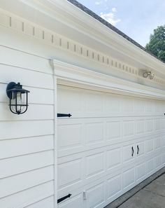 two white garage doors on the side of a house with black handles and knobs