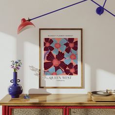 a poster hangs on the wall next to a red cabinet and blue vase with flowers