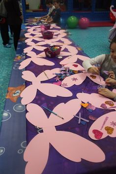 children are sitting at a long table with paper cut outs on it, making crafts