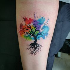 a colorful tree tattoo on the arm with watercolor splatters and roots painted all over it