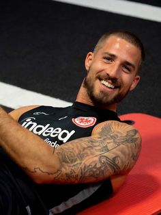 a man sitting on top of a surfboard with tattoos on his arms and chest