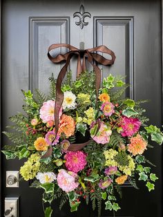 a wreath on the front door with flowers and greenery hanging from it's side