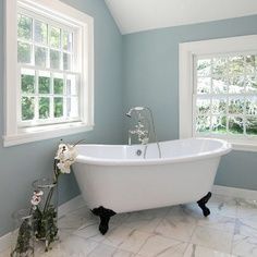 a white bath tub sitting under two windows in a bathroom