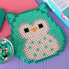 an owl bead pattern next to a bowl of beads and a craft kit on a purple surface