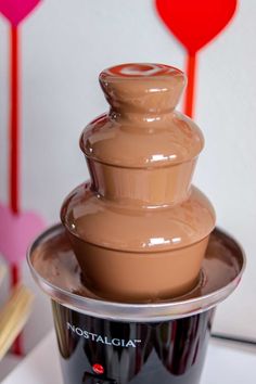 a chocolate fountain is sitting on top of a table next to a red heart shaped balloon