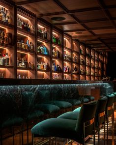 a dimly lit bar with green velvet chairs and shelves full of liquor bottles on the wall