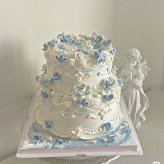 a wedding cake with blue and white flowers on top is sitting on a platter