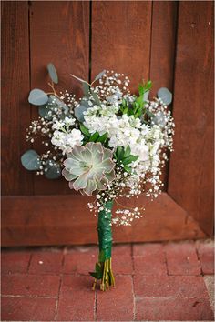 a bouquet of white flowers sitting on top of a brick floor next to a wooden door