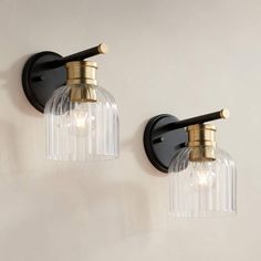 two lights are attached to the wall with clear glass shades and brass fixtures on each side