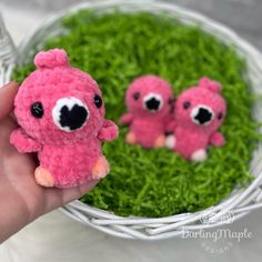 two small pink stuffed animals sitting on top of green grass in front of a basket