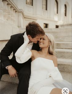 a man and woman are sitting on the steps in front of a building smiling at each other