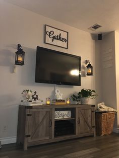 a flat screen tv mounted on the wall above a wooden cabinet with baskets and candles